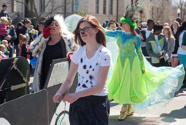 Photo of a group of people walking in the parade dressed up. A young woman in the foreground is wearing facepaint so she looks like a puppy.